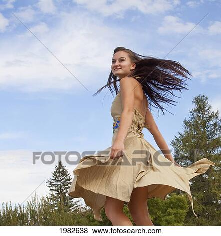 Stock Photo - a young woman dancing in a park with a flowing dress; edmonton alberta canada. Fotosearch