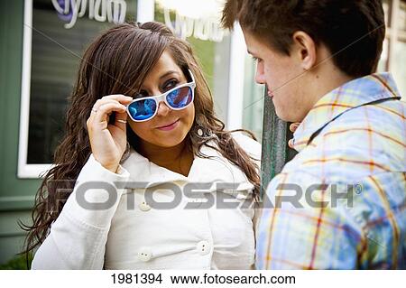 a young woman looks over rim of her sunglasses at a young man; bellingham washington united states of america View Large Photo Image Picture - a young woman looks over rim of her sunglasses at a young man; bellingham washington united states of america. Fotosearch