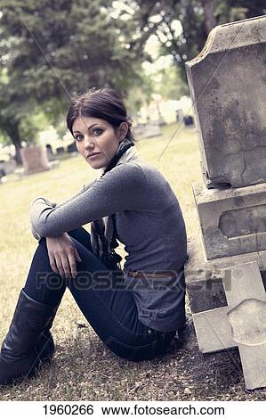 Stock Photograph - a young woman sitting against a tombstone; edmonton, alberta, canada. Fotosearch