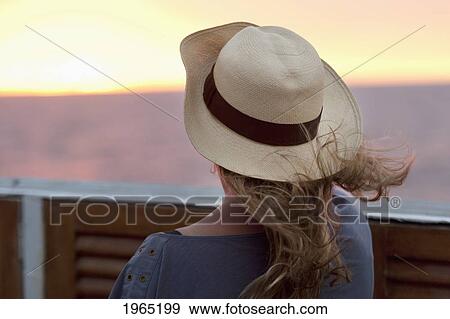Stock Photo - a young woman wearing a hat and watching the sunset; galapagos equador. Fotosearch