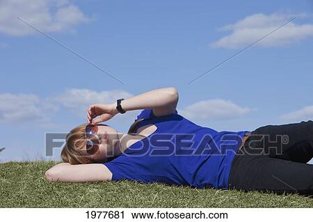 Stock Image - a young woman wearing sunglasses laying on the grass; edmonton alberta canada. Fotosearch