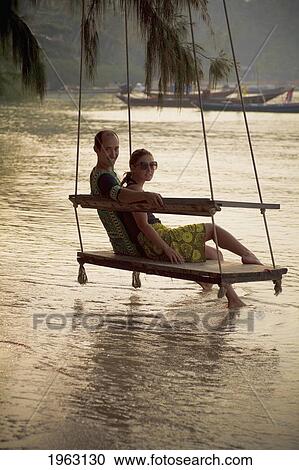 couple sits on beach swing at sunset; koh tao, thailand View Large Photo Image Stock Image - couple sits on beach swing at sunset; koh tao, thailand. Fotosearch