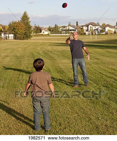 Stock Image - father and son playing football in a park; beaumont alberta canada. Fotosearch