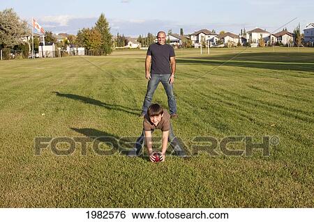 Stock Photograph - father and son playing football in a park; beaumont alberta canada. Fotosearch