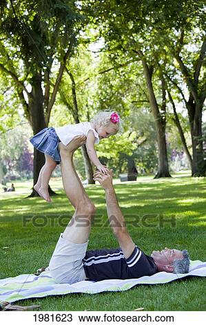 Stock Image - father lifting daughter up on his legs in the park; edmonton alberta canada. Fotosearch