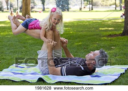 Stock Photo - father lifting daughter up on his legs in the park; edmonton alberta canada. Fotosearch