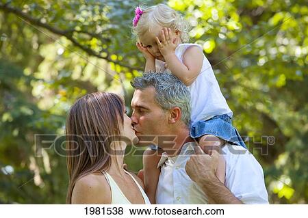 Stock Photo - husband and wife kissing in front of toddler; edmonton alberta canada. Fotosearch