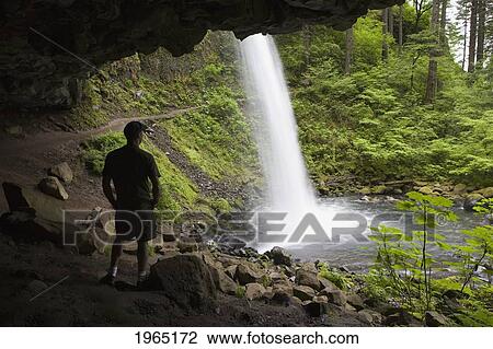 male hiker standing under a cliff overlooking a waterfall; oregon united states of america View Large Photo Image Stock Image - male hiker standing under a cliff overlooking a waterfall; oregon united states of america. Fotosearch
