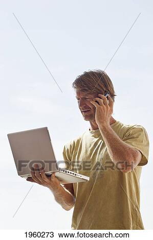 man reading screen of his laptop computer while speaking on a cell phone; torremolinos, malaga, andalusia, spain View Large Photo Image Stock Image - man reading screen of his laptop computer while speaking on a cell phone; torremolinos, malaga, andalusia, spain. Fotosearch