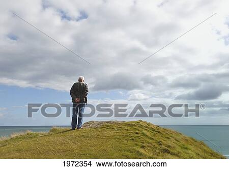 man standing alone on a hill staring at the ocean at inchydoney beach near clonakilty; county cork ireland View Large Photo Image Picture - man standing alone on a hill staring at the ocean at inchydoney beach near clonakilty; county cork ireland. Fotosearch
