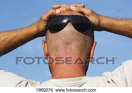 Stock Photography - man wearing sun glasses on the back of his shaven head and with his hands resting on top of his head; spain. Fotosearch