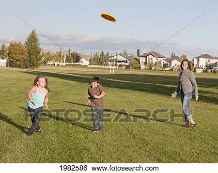 Stock Photograph - mother throwing flying disc to children in a park; beaumont alberta canada. Fotosearch