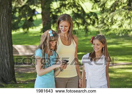 Stock Image - mother walking with two daughters and laughing at text messages; edmonton alberta canada. Fotosearch