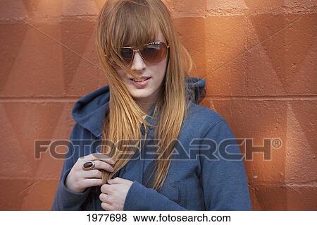 portrait of a young woman wearing sunglasses and standing against a wall; edmonton alberta canada View Large Photo Image Stock Photo - portrait of a young woman wearing sunglasses and standing against a wall; edmonton alberta canada. Fotosearch