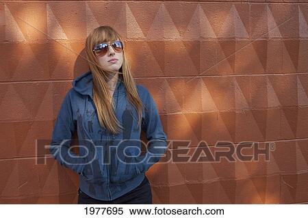portrait of a young woman wearing sunglasses and standing against a wall; edmonton alberta canada View Large Photo Image Stock Photography - portrait of a young woman wearing sunglasses and standing against a wall; edmonton alberta canada. Fotosearch