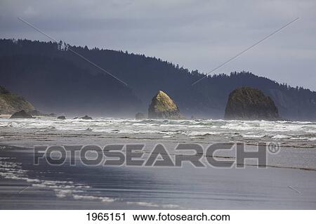 Stock Image - rock formations in the ocean with waves on the beach; cannon beach oregon united states of america. Fotosearch