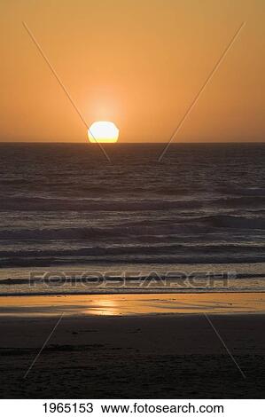 Stock Image - silhouette of the ocean with the sun setting on the horizon reflected in the ocean; newport oregon united states of america. Fotosearch