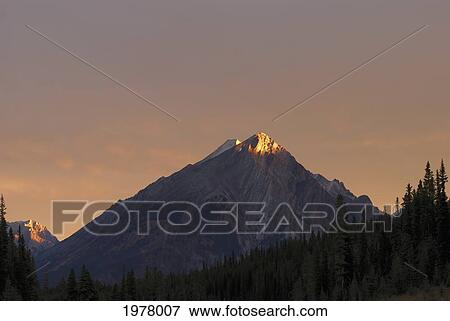Stock Photo - sunrise lights up a mountain peak; alberta canada. Fotosearch