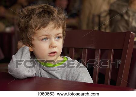 Stock Image - toddler boy sitting in a restaurant chair looking out the window; st. albert, alberta, canada. Fotosearch