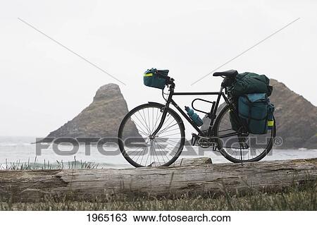 Stock Image - touring bicycle with full bags on a beach with rock formation in the ocean in the background; heceta head oregon united states of america. Fotosearch