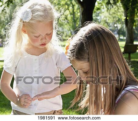 Stock Image - two sisters looking at an insect; edmonton alberta canada. Fotosearch