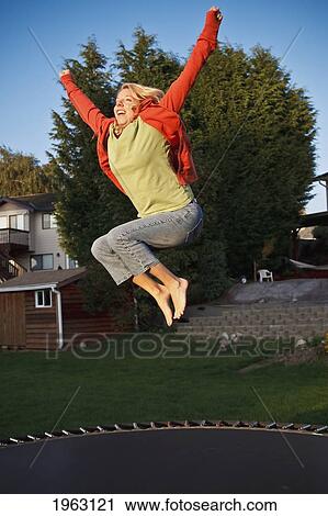 Stock Image - woman jumps on a trampoline with arms raised; ferndale, washington, united states of america. Fotosearch