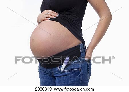 Stock Photo - A bare pregnant belly with a pregnancy test in the pants pocket; edmonton alberta canada. Fotosearch