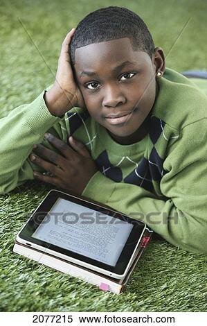 Stock Photography - A boy in an argyle sweater lays on the grass reading from an electronic notebook; portland oregon united states of america. Fotosearch