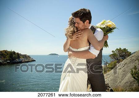 A bride and groom embrace at the water's edge in whytecliff park; vancouver british columbia canada View Large Photo Image Stock Image - A bride and groom embrace at the water's edge in whytecliff park; vancouver british columbia canada. Fotosearch