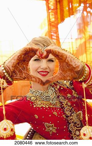 Stock Photograph - A bride wearing an ornate gown and jewelry making a heart shape with her hands covered in mehndi; ludhiana punjab india. Fotosearch