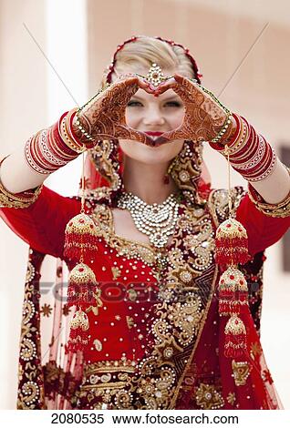 A bride with blond hair wearing a red and gold sari and jewelry holding her mehndi covered hands in a heart shape; ludhiana punjab india View Large Photo Image Stock Photography - A bride with blond hair wearing a red and gold sari and jewelry holding her mehndi covered hands in a heart shape; ludhiana punjab india. Fotosearch