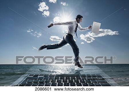 Stock Image - A businessman running across the water on top of a large computer holding a briefcase and cellphone; tarifa cadiz andalusia spain. Fotosearch