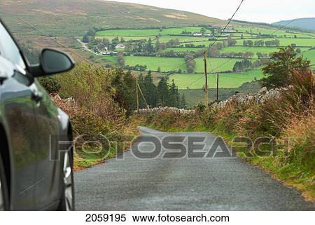 Stock Photography - A Car Travels Down A Paved Road; Ireland. Fotosearch