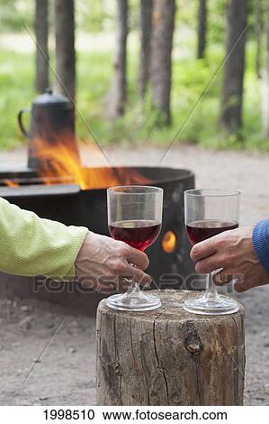 A Couple Holding Wine Glasses On A Block Of Wood With A Fire Pit Burning In A Campground; Waterton Alberta Canada View Large Photo Image Stock Image - A Couple Holding Wine Glasses On A Block Of Wood With A Fire Pit Burning In A Campground; Waterton Alberta Canada. Fotosearch