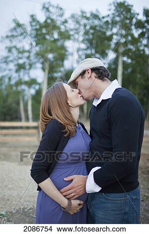 Picture - A couple kissing with their hands on her pregnant belly; sherwood park alberta canada. Fotosearch