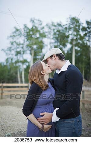 Stock Image - A couple kissing with their hands on her pregnant belly; sherwood park alberta canada. Fotosearch