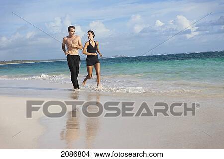 Picture - A couple runs together on the beach; punta cana la altagracia dominican republic. Fotosearch