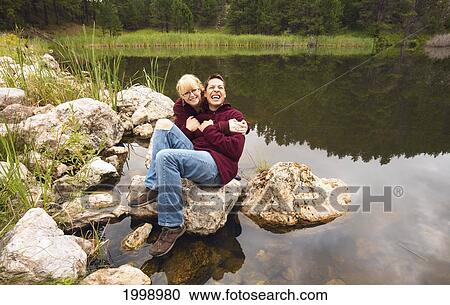 A Couple Sitting On A Rock At The Water's Edge In Laughter; Black Hills South Dakota United States Of America View Large Photo Image Stock Image - A Couple Sitting On A Rock At The Water's Edge In Laughter; Black Hills South Dakota United States Of America. Fotosearch
