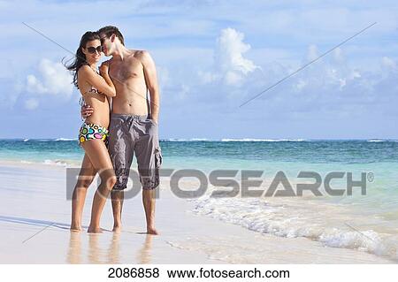 A couple wearing swimsuits stand on the beach at the water's edge in an embrace; punta cana la altagracia dominican republic View Large Photo Image Stock Photo - A couple wearing swimsuits stand on the beach at the water's edge in an embrace; punta cana la altagracia dominican republic. Fotosearch