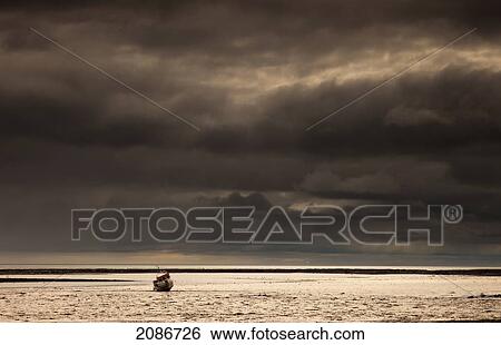 Stock Photograph - A fishing boat out in the water under dark storm clouds; boulmer northumberland england. Fotosearch