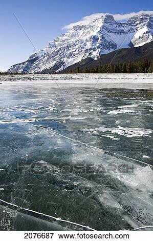 A frozen mountain lake snow free with cracks and snow covered mountain in the background with blue sky; banff alberta canada View Large Photo Image Stock Photo - A frozen mountain lake snow free with cracks and snow covered mountain in the background with blue sky; banff alberta canada. Fotosearch