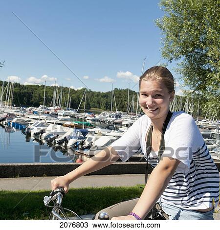 Stock Image - A girl on a bike with boats in the harbour in the background; oslo norway. Fotosearch