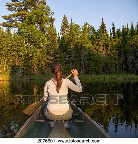 A girl paddles a boat on a tranquil lake; lake of the woods ontario canada View Large Photo Image Stock Image - A girl paddles a boat on a tranquil lake; lake of the woods ontario canada. Fotosearch