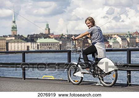 Stock Photo - A girl riding a bicycle on a path along the water's edge; stockholm sweden. Fotosearch