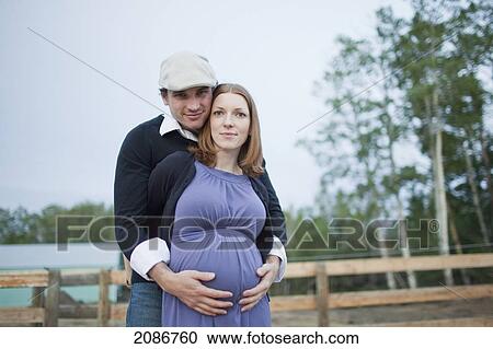 Stock Image - A husband embraces his wife and her pregnant belly; sherwood park alberta canada. Fotosearch