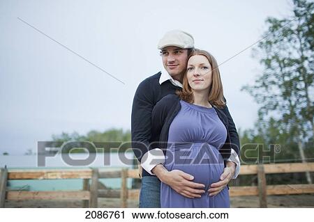 Stock Image - A husband embraces his wife and her pregnant belly; sherwood park alberta canada. Fotosearch
