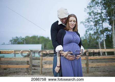Stock Photo - A husband embraces his wife and her pregnant belly; sherwood park alberta canada. Fotosearch