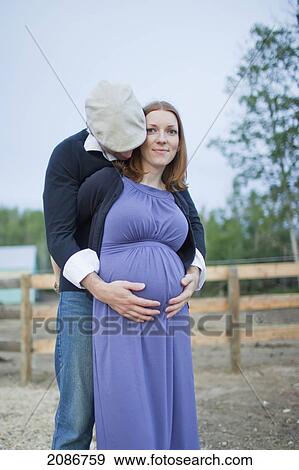 Stock Photo - A husband embraces his wife and her pregnant belly; sherwood park alberta canada. Fotosearch