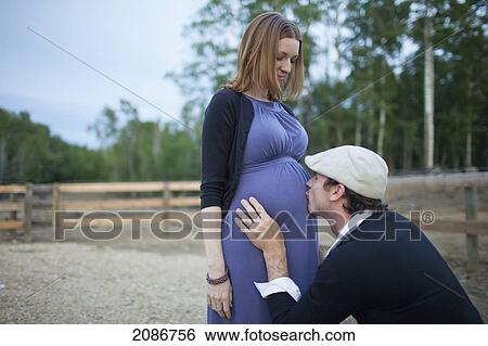 Stock Photograph - A husband kissing his wife's pregnant belly; sherwood park alberta canada. Fotosearch