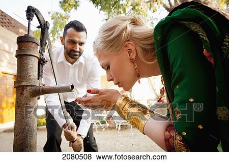 A man pumping water from a well as a blond woman in a sari drinks from her cupped hands; ludhiana punjab india View Large Photo Image Stock Photo - A man pumping water from a well as a blond woman in a sari drinks from her cupped hands; ludhiana punjab india. Fotosearch